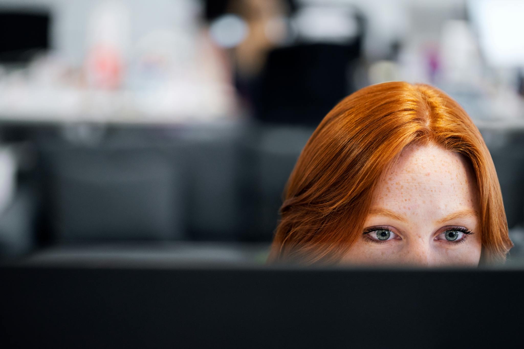 A woman with red hair intensely focused on a computer screen in an office setting.