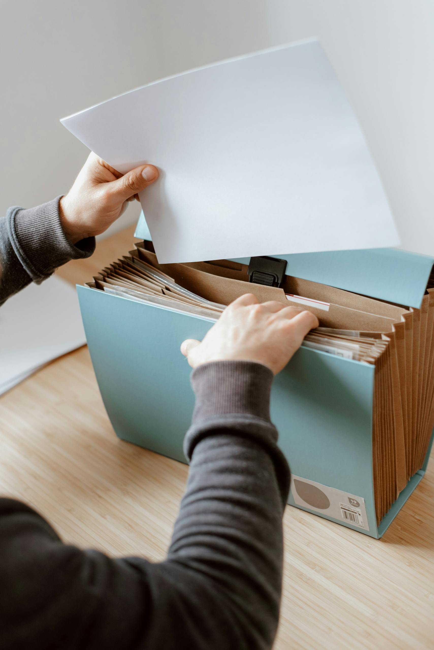 Crop anonymous male putting blank sheet of paper in case placed on wooden table